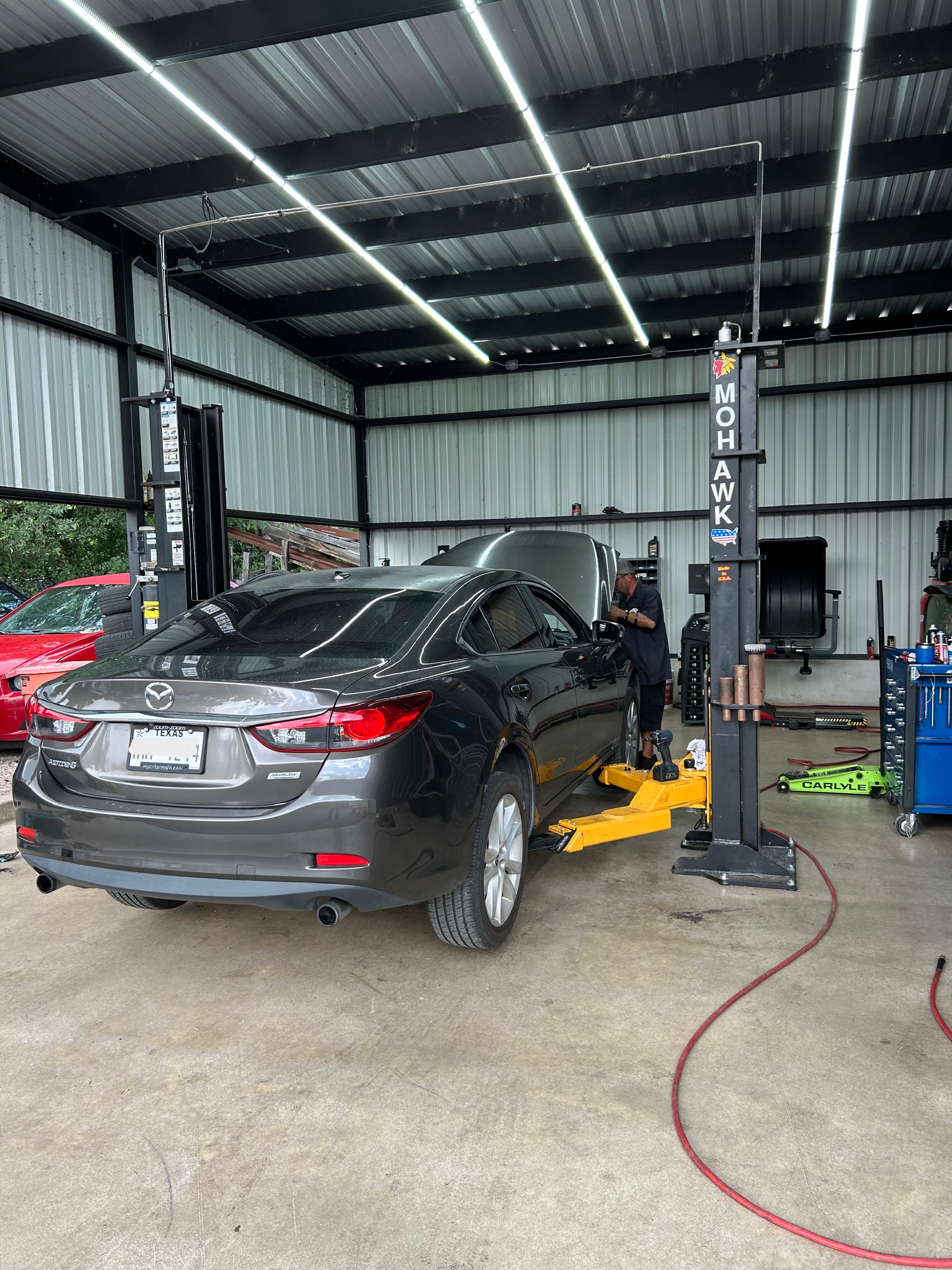 Technician inspecting a Mazda6 on a lift inside the Thomas' Mustang Lube & Auto Repair shop in Kingsland, TX