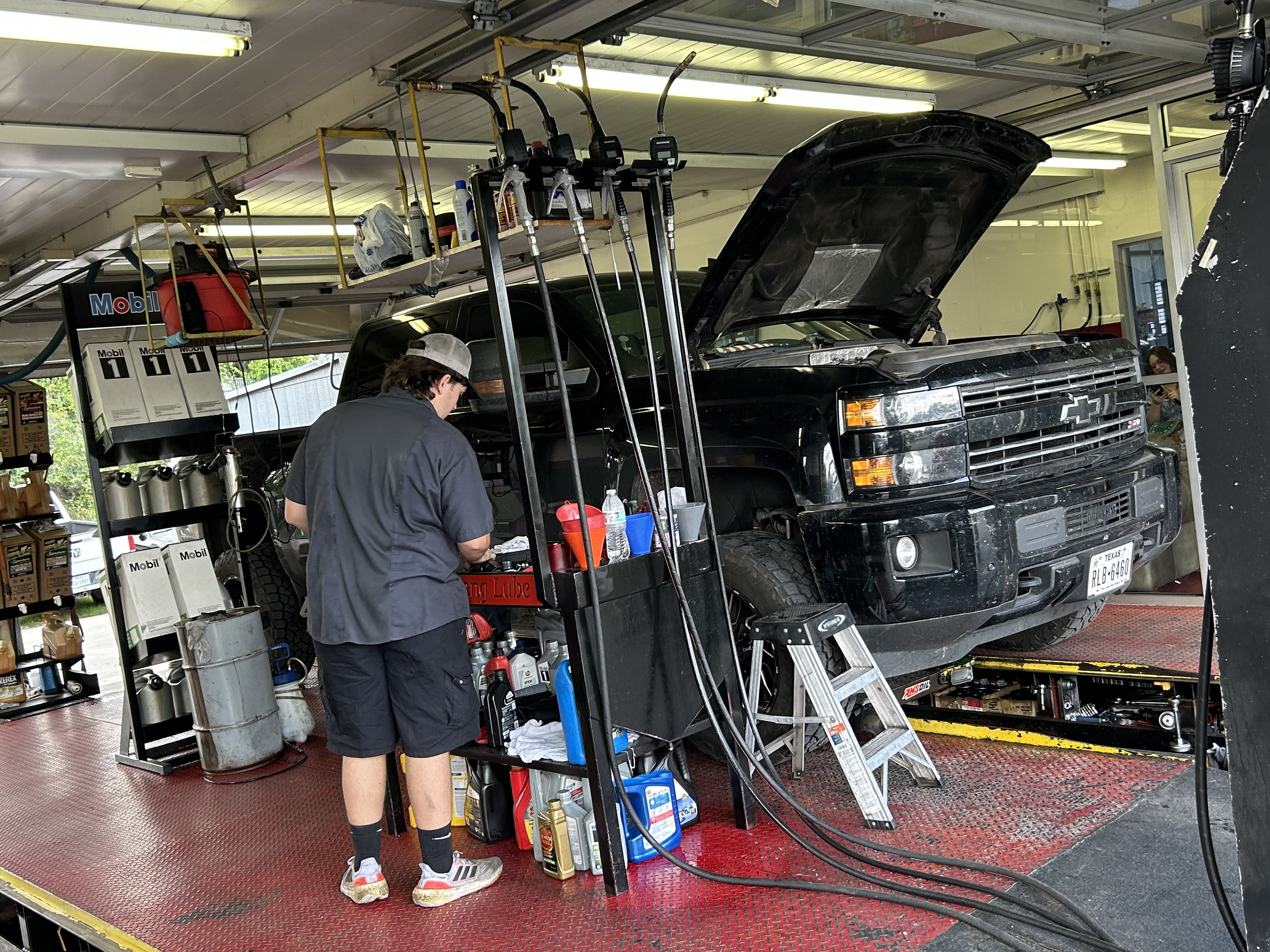 Technician performing an oil change on a lifted Chevrolet pickup at Thomas' Mustang Lube & Auto Repair in Kingsland, TX